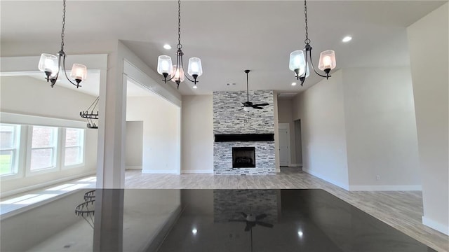 kitchen featuring ceiling fan with notable chandelier, a stone fireplace, light wood-type flooring, and hanging light fixtures