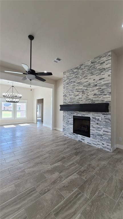 unfurnished living room with a fireplace and ceiling fan with notable chandelier