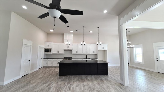 kitchen featuring ceiling fan with notable chandelier, a kitchen island, light hardwood / wood-style flooring, white cabinetry, and stainless steel microwave