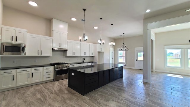 kitchen with sink, appliances with stainless steel finishes, decorative light fixtures, a kitchen island, and white cabinetry