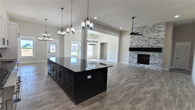 kitchen featuring ceiling fan, hanging light fixtures, a kitchen island, a fireplace, and white cabinets