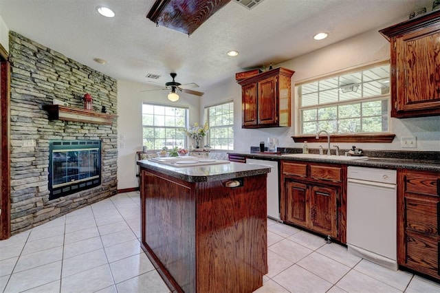 kitchen featuring dishwasher, ceiling fan, light tile patterned floors, a fireplace, and a kitchen island