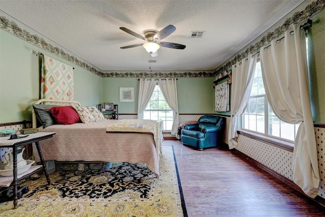 bedroom with a textured ceiling, ceiling fan, and dark hardwood / wood-style floors