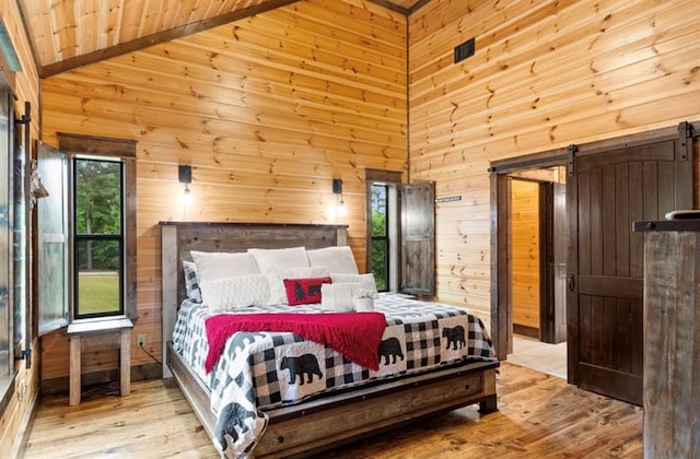 bedroom featuring wooden ceiling, high vaulted ceiling, wooden walls, a barn door, and light hardwood / wood-style floors