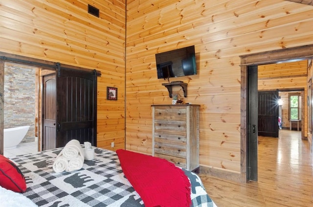 bedroom with wooden walls, a barn door, light wood-type flooring, and connected bathroom