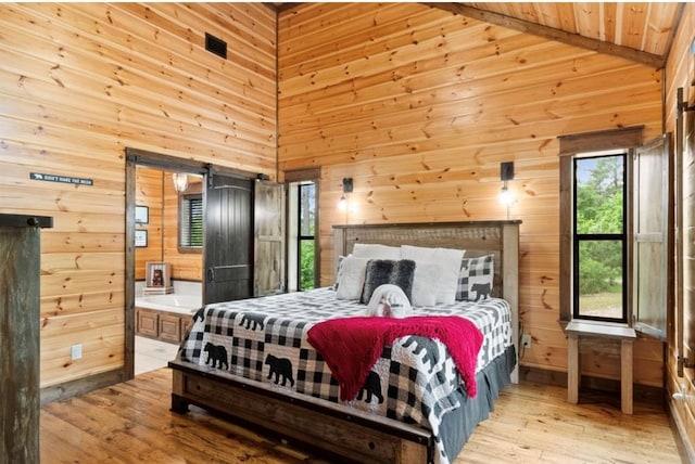 bedroom with wood walls, ensuite bathroom, a barn door, and light hardwood / wood-style flooring