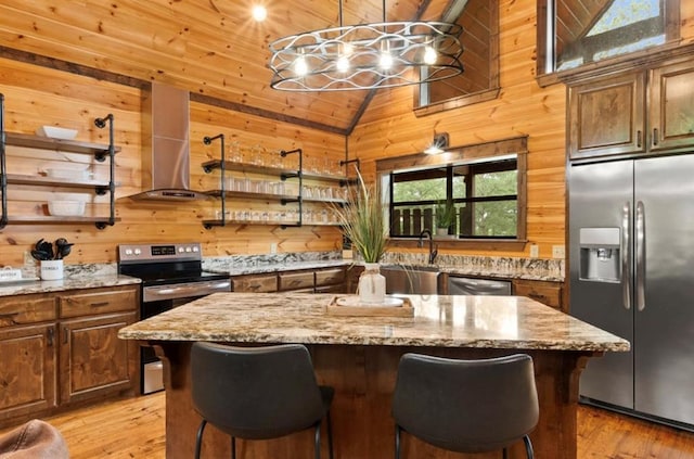 kitchen with wood walls, a kitchen island, a breakfast bar area, and appliances with stainless steel finishes