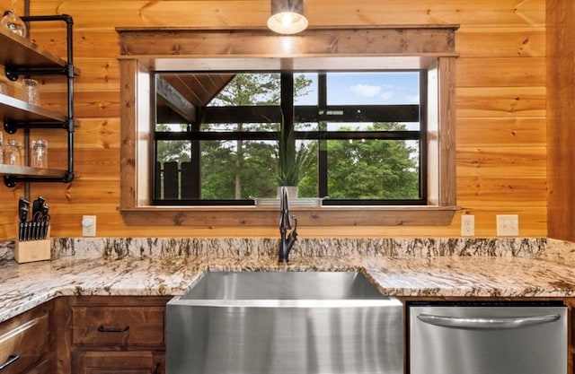 kitchen with dishwasher, light stone countertops, and wooden walls