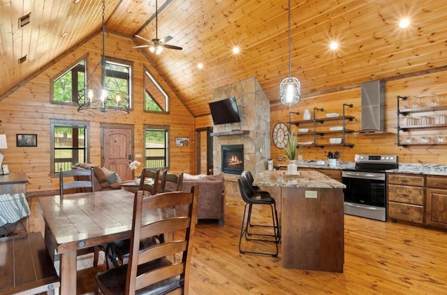 dining area with wood walls, high vaulted ceiling, a stone fireplace, light wood-type flooring, and wood ceiling