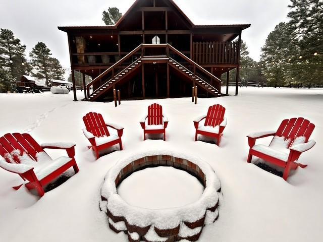 snow covered back of property with a fire pit and stairs
