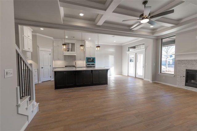 kitchen with white cabinets, stainless steel microwave, an island with sink, and hanging light fixtures