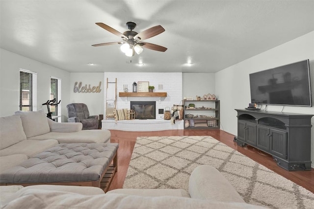 living room with ceiling fan, a large fireplace, and dark hardwood / wood-style floors