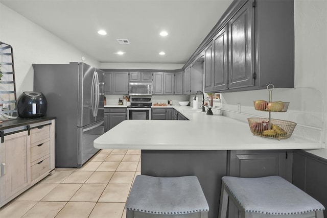 kitchen with kitchen peninsula, gray cabinetry, stainless steel appliances, light tile patterned floors, and a breakfast bar area