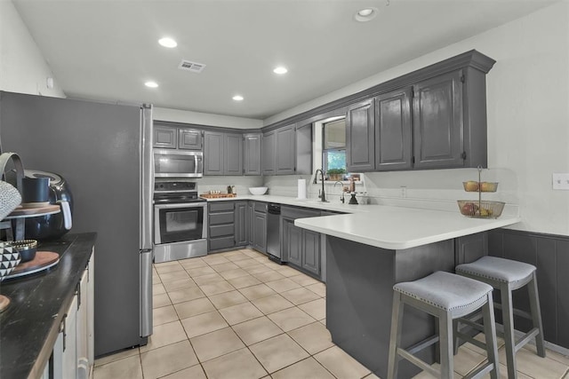 kitchen featuring gray cabinetry, sink, a kitchen bar, kitchen peninsula, and stainless steel appliances