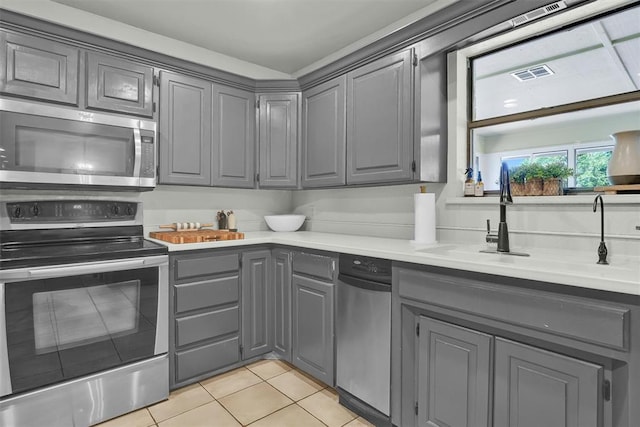 kitchen featuring gray cabinetry, sink, light tile patterned floors, and appliances with stainless steel finishes