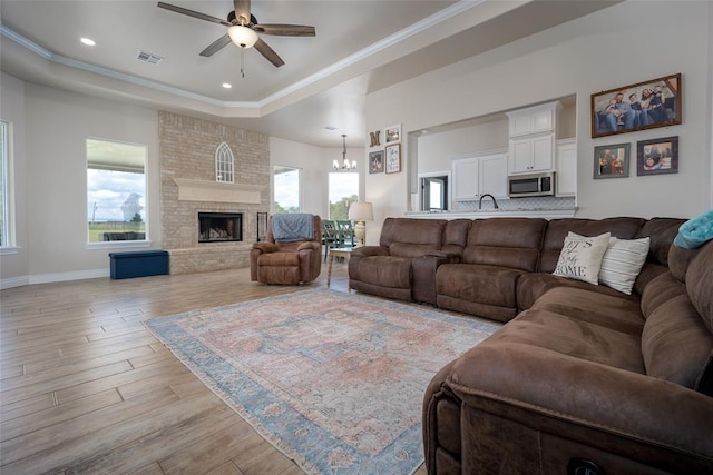 living room featuring ceiling fan with notable chandelier, a healthy amount of sunlight, a raised ceiling, and light wood-type flooring