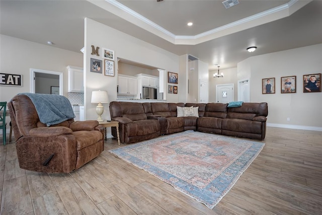 living room with a tray ceiling, light hardwood / wood-style flooring, a notable chandelier, and ornamental molding