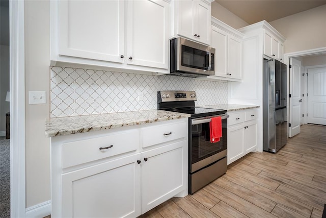 kitchen featuring light stone counters, light hardwood / wood-style flooring, backsplash, white cabinets, and appliances with stainless steel finishes