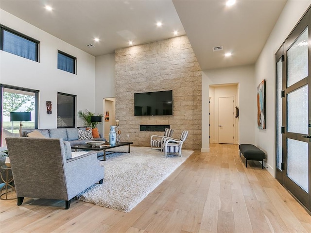 living room with a stone fireplace, light wood-type flooring, and a high ceiling