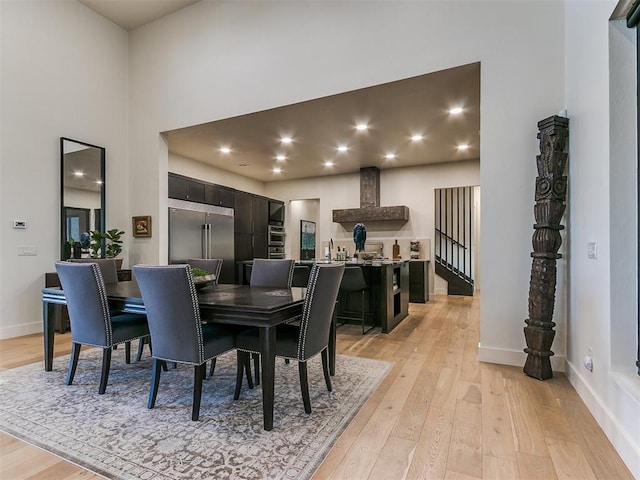 dining space with light hardwood / wood-style floors, a towering ceiling, and sink