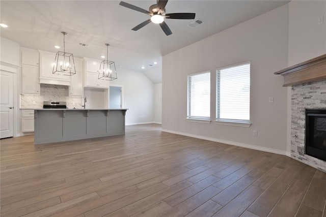 unfurnished living room featuring ceiling fan, lofted ceiling, a fireplace, and light hardwood / wood-style flooring