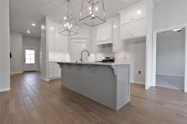 kitchen featuring custom exhaust hood, hanging light fixtures, an island with sink, stainless steel range, and white cabinetry