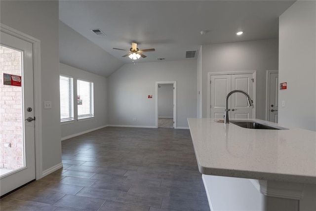 kitchen featuring light stone countertops, ceiling fan, sink, a center island with sink, and lofted ceiling