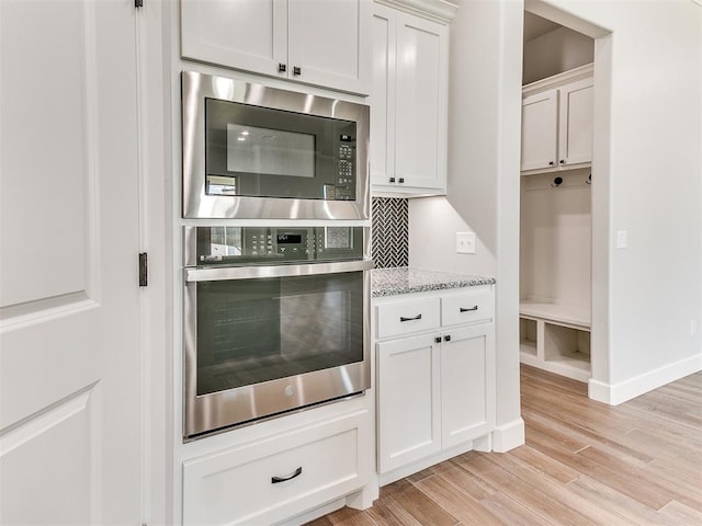 kitchen featuring light stone countertops, white cabinetry, stainless steel appliances, backsplash, and light hardwood / wood-style floors