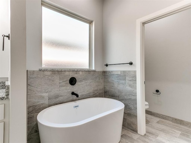 bathroom featuring a bathtub, toilet, and tile walls