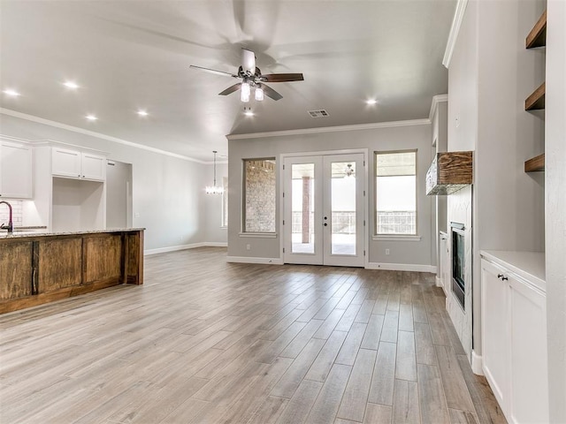 unfurnished living room featuring ceiling fan with notable chandelier, light hardwood / wood-style floors, ornamental molding, and sink