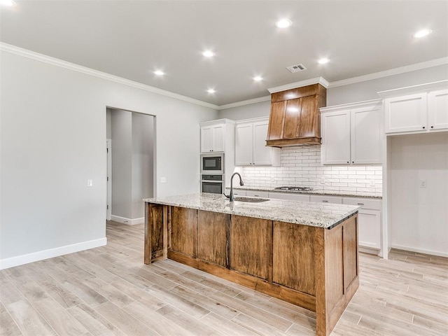 kitchen with light stone countertops, sink, premium range hood, an island with sink, and white cabinets