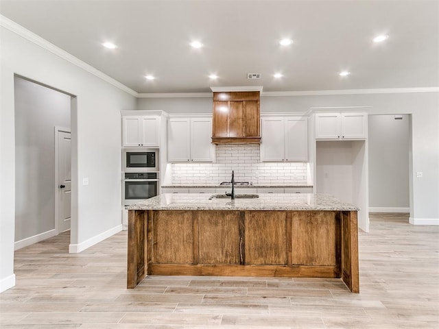 kitchen with sink, stainless steel appliances, light stone counters, a kitchen island with sink, and white cabinets