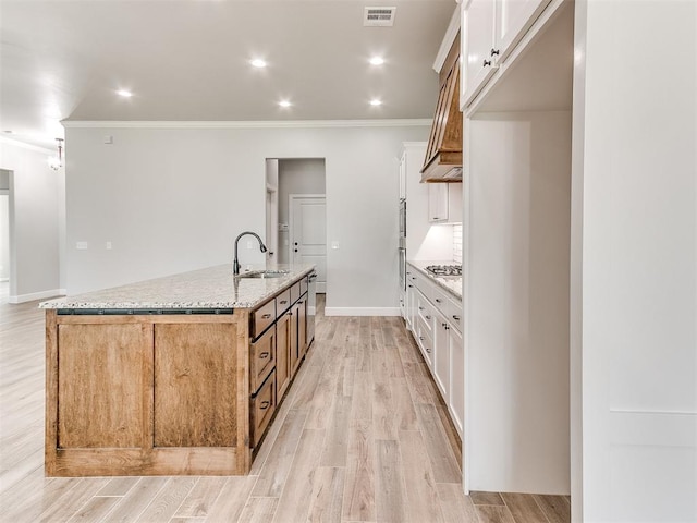 kitchen with light stone countertops, light wood-type flooring, sink, a large island with sink, and white cabinetry