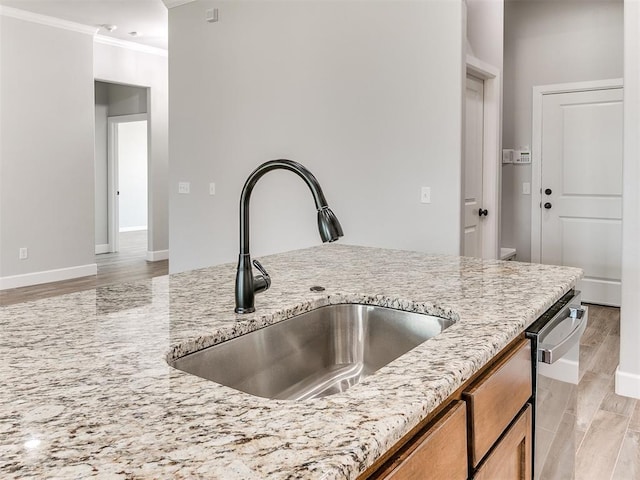 kitchen featuring dishwasher, sink, light hardwood / wood-style flooring, ornamental molding, and light stone countertops