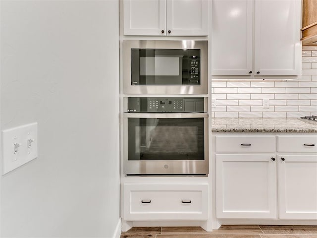 kitchen with black microwave, stainless steel oven, white cabinets, and light stone countertops