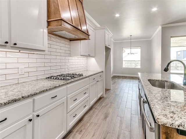 kitchen with white cabinets, sink, appliances with stainless steel finishes, decorative light fixtures, and custom range hood