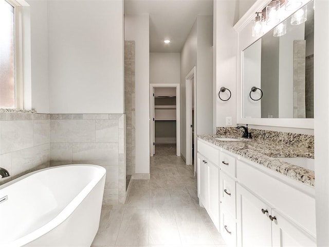 bathroom featuring tile patterned flooring, a bath, vanity, and tile walls