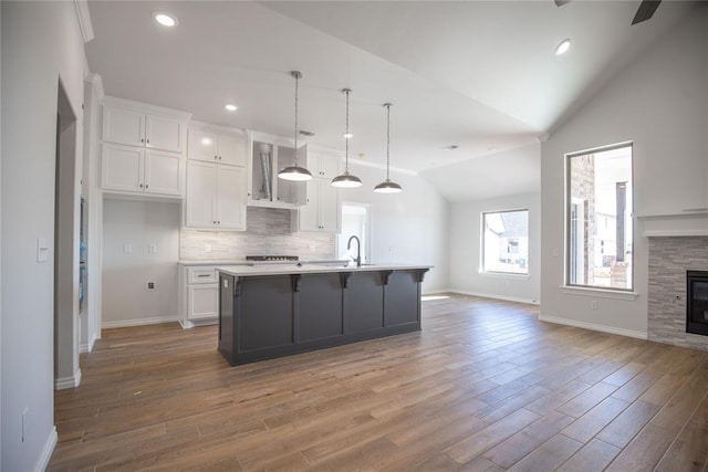 kitchen featuring white cabinetry, hardwood / wood-style floors, an island with sink, and vaulted ceiling