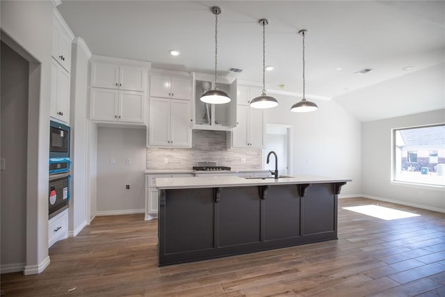 kitchen with sink, dark wood-type flooring, pendant lighting, a kitchen island with sink, and appliances with stainless steel finishes