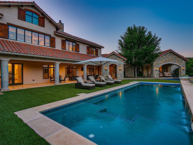 back house at dusk with pool water feature, a patio area, and a yard