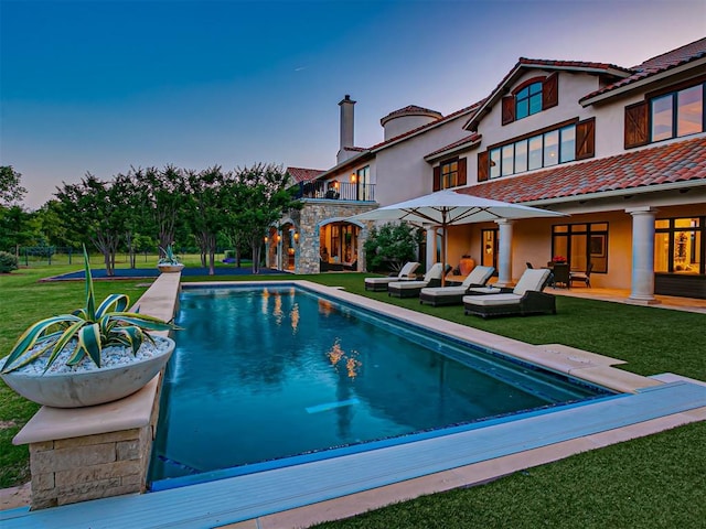 pool at dusk featuring a lawn