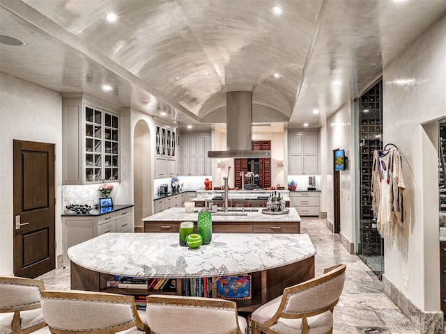 kitchen with a breakfast bar area, a large island with sink, island range hood, and lofted ceiling