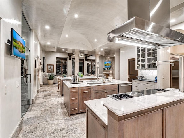 kitchen with sink, decorative columns, a large island with sink, stainless steel stovetop, and island range hood