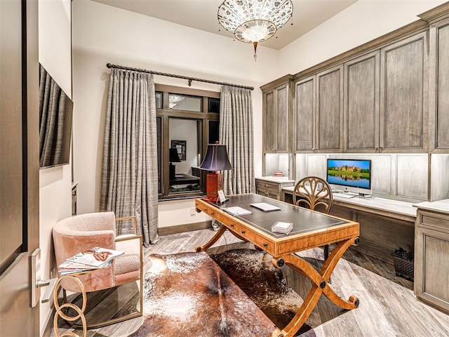 office area featuring an inviting chandelier, built in desk, and light hardwood / wood-style floors