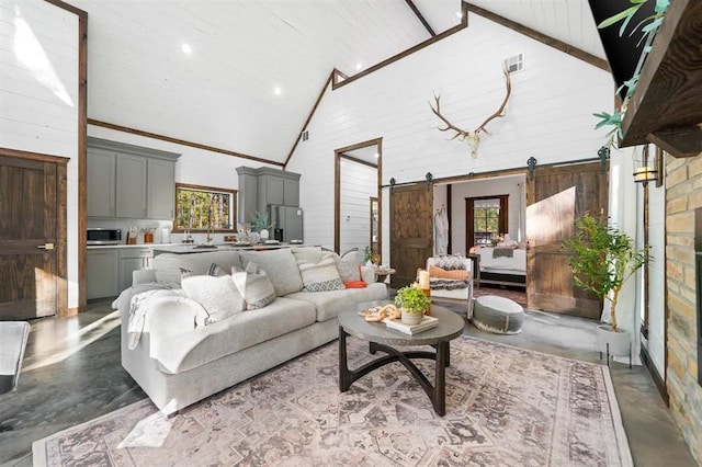 living room featuring concrete flooring, a barn door, high vaulted ceiling, and a wealth of natural light