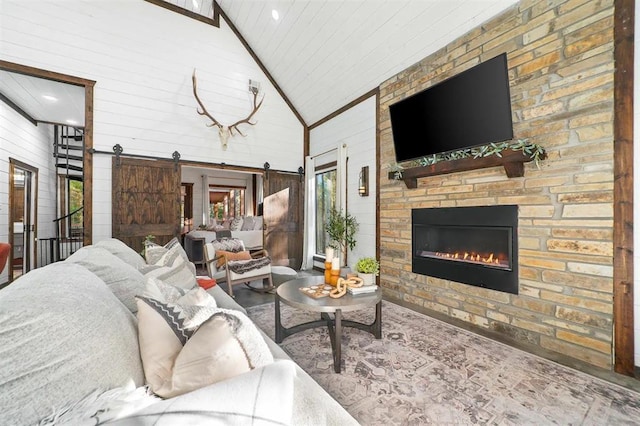 living room featuring a barn door, high vaulted ceiling, a stone fireplace, and wood walls