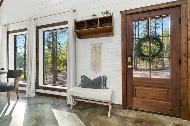 doorway with concrete flooring, plenty of natural light, and wooden walls