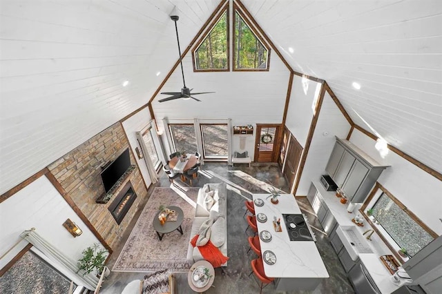 living room with ceiling fan, a stone fireplace, and high vaulted ceiling