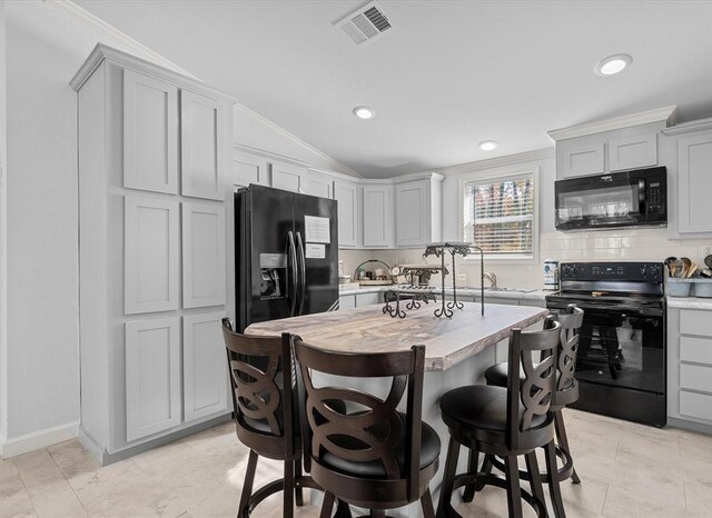 kitchen featuring crown molding, vaulted ceiling, a kitchen island, and black appliances