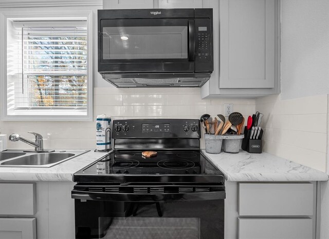 kitchen featuring tasteful backsplash, light stone countertops, sink, and black appliances